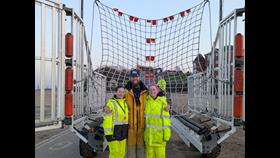 Faye, Lisa and Ben pose, smiling, in front of a recovery net fully rigged inside the recovery carriage for the RNLI.