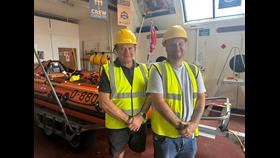 picture of two men stood beside an RNLI D class lifeboat