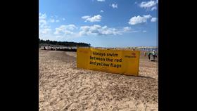 Always swim between the red and yellow flags sign on Wells beach with beach huts and beach in backgroun