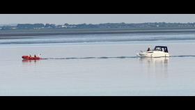 An inshore lifeboat is bringing in a motor cruiser into sheltered sea conditions