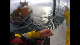 An RNLI crew member on board the yacht takes the tow line from the crew on the All-Weather Lifeboat.