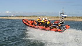RNLI orange Atlantic 85 rib with four boat crew in yellow and black heading out to sea with white wake behind the boat.
