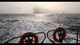 A vessel billowing smoke is on the horizon. Photo take at sea with two orange life buoys in the foreground.