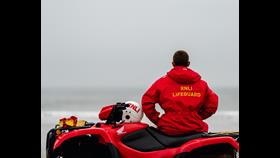 RNLI Lifeguard Scarborough quad patrol. Lifeguard facing the sea sat on the RNLI quad bike in full uniform with helmet on the quad