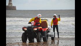 Lifeguard Supervisor Training at Roker Sunderland two Lifeguards in full RNLI lifeguard kit with RNLI quad bike on shore line. Lighthouse and sea in background