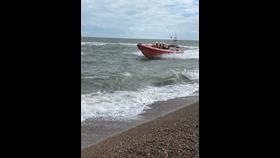 RNLI lifeboat Ralph welcomed to Aldeburgh in official naming ceremony Lifebaot with volunteer crew in water and shingle beach in foreground