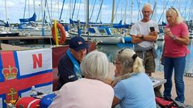 Person wearing lifejacket talking to others in front of an RNLI flag