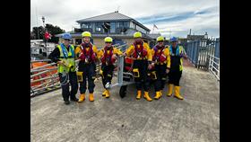 Six members of RNLI Fleetwood's volunteer crew, with Fleetwood Lifeboat Station in the background.