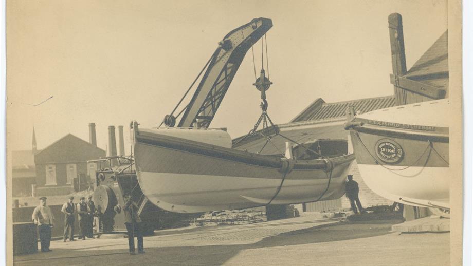 Black and white image of lifeboat being hoisted by crane