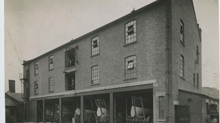 Black and white image of boatshed exterior, four lifeboats on cradles with workmen
