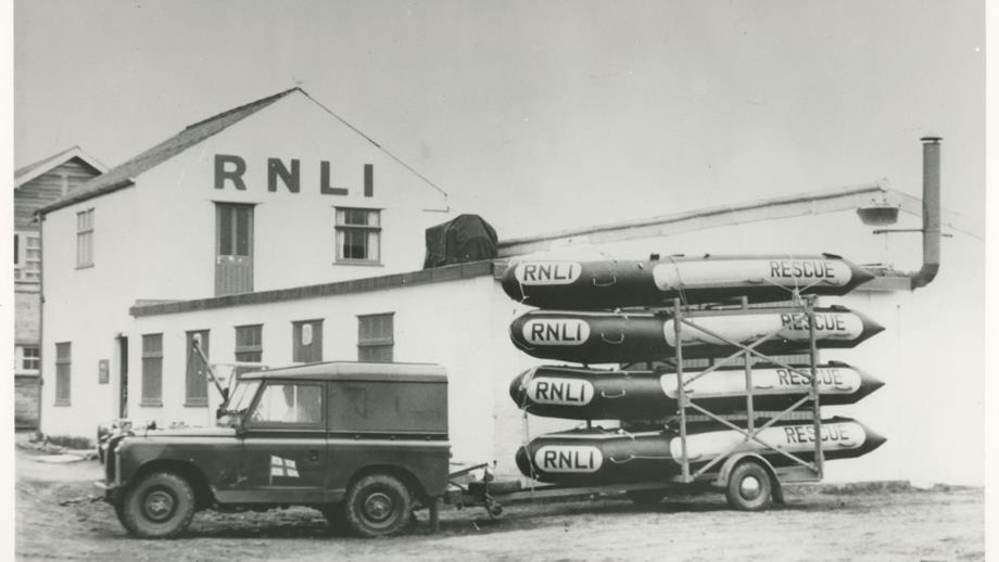 Black and white image of landrover with four inflatable rescue boats on trailer
