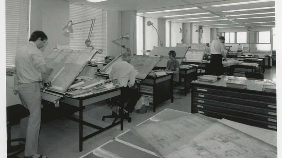 Black and white image of drawing office interior with staff at drawing boards