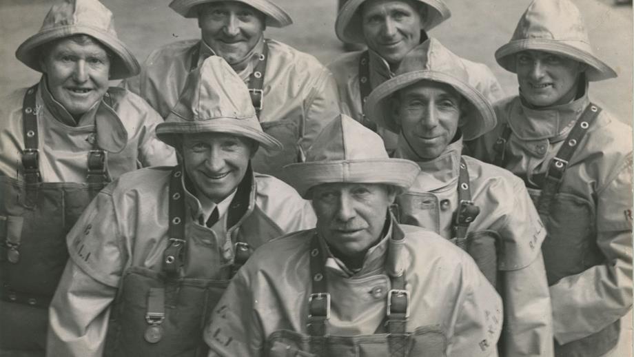 Black and white image of seven men in crew kit with medals