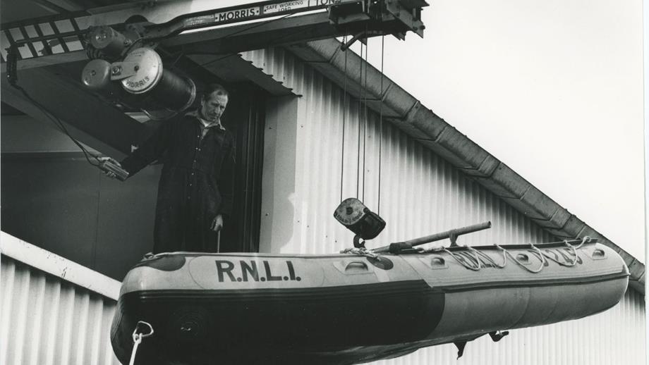 Black and white image of inflatable lifeboat being hoisted