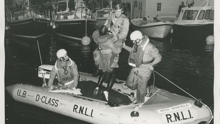 Black and white image of crew member being lifted from inshore lifeboat