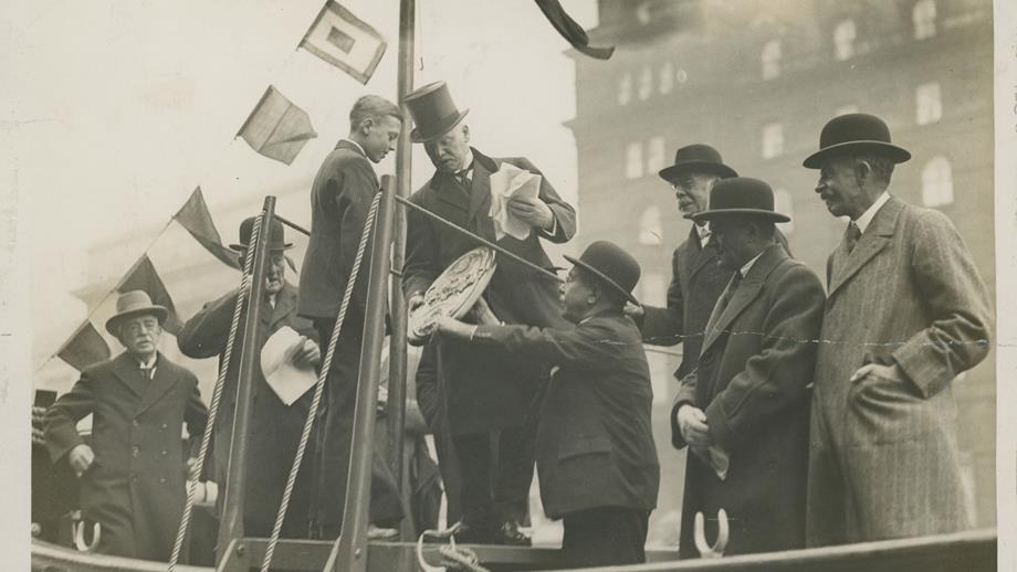 Black and white image of boy being presented with competition shield onboard lifeboat