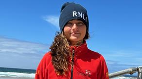 RNLI Lifeguard Elise Irish smiling, with blue skies and the sea in the background.