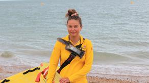 RNLI Lifeguard Georgia Laing in a lifeguard kit smiling at a sandy beach