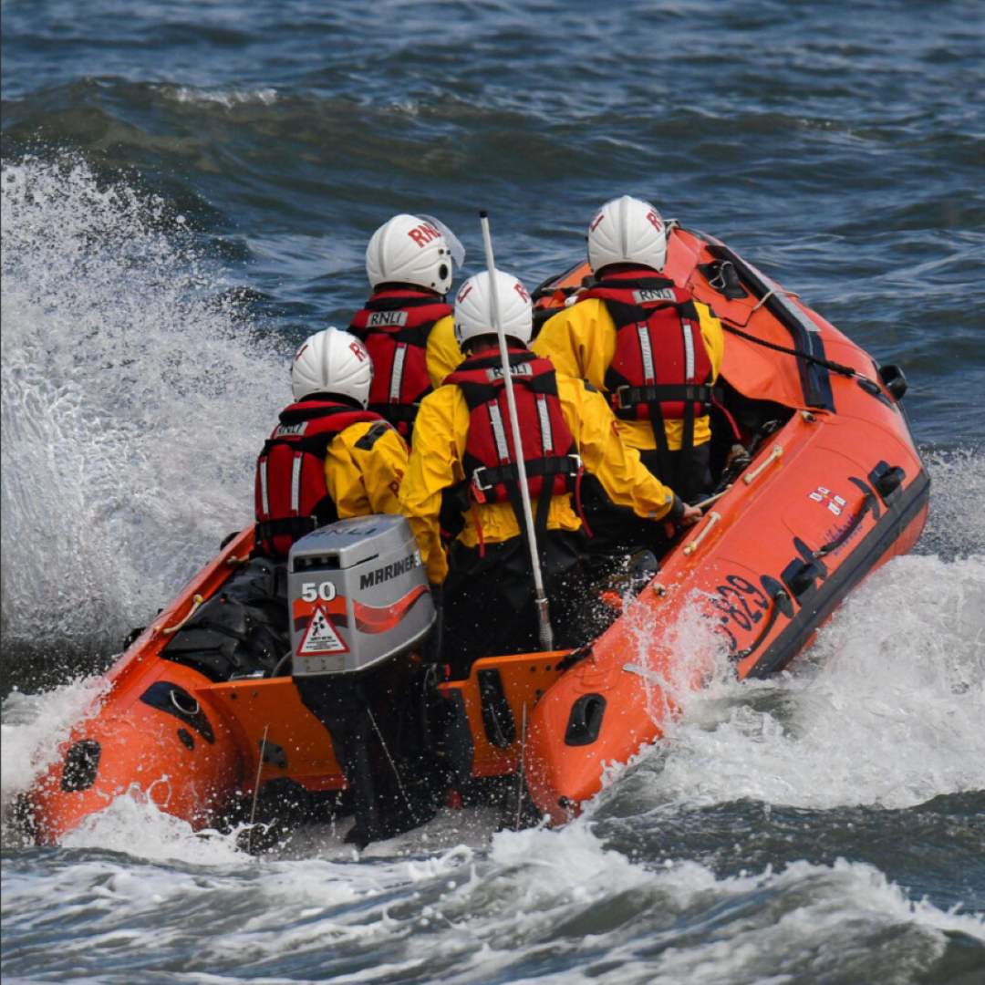 Tynemouth’s D class inshore lifeboat, with four crew members onboard, heading out to sea. The lifeboat is creating splash as it powers through the water.