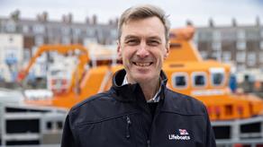 Smiling headshot of Peter Sparkes, RNLI CEO, standing in front boat in black jacket.