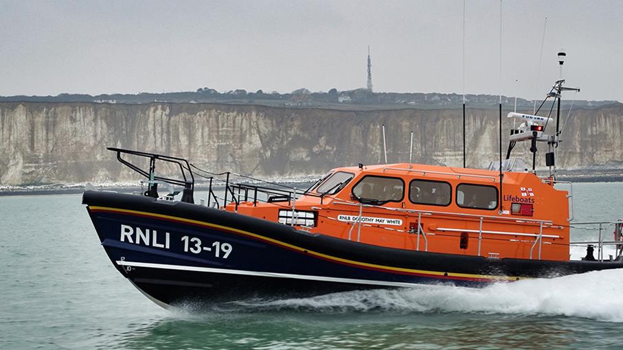 Workington Shannon class lifeboat at sea on a cloudy day with cliffs in the background.
