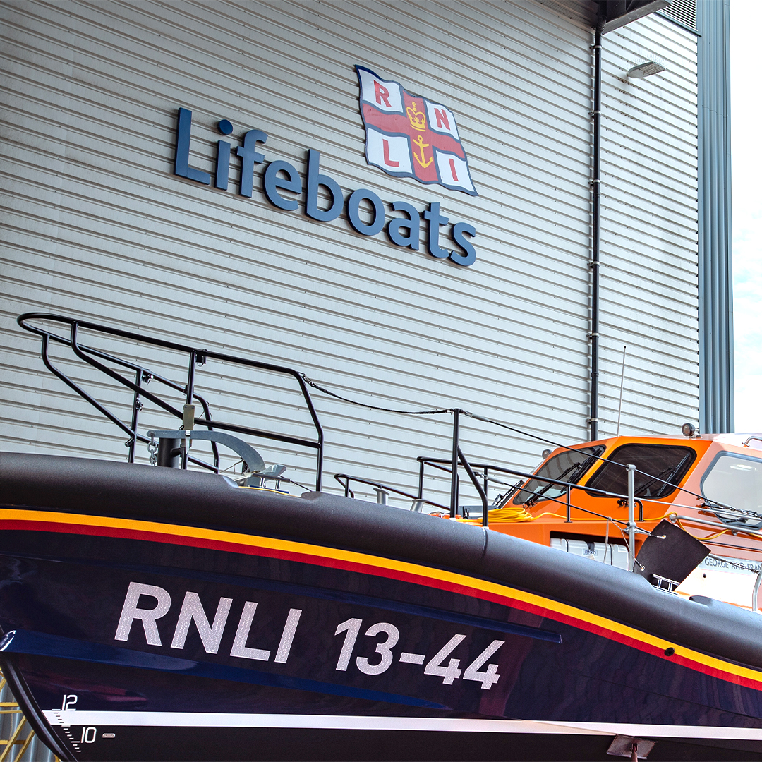 An RNLI Shannon class lifeboat sits in the yard at the All-weather Lifeboat Centre lifeboat factory beneath the RNLI lifeboats logo.