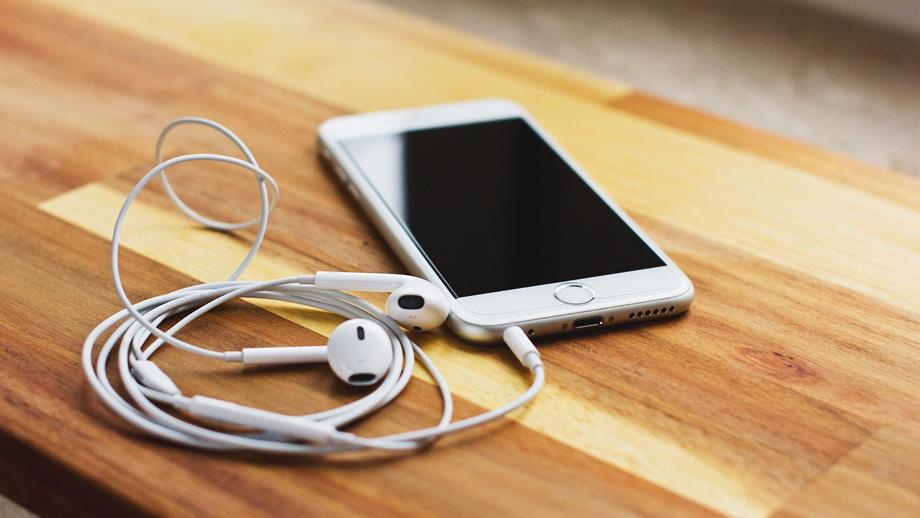 A white mobile phone with headphones on a wooden table