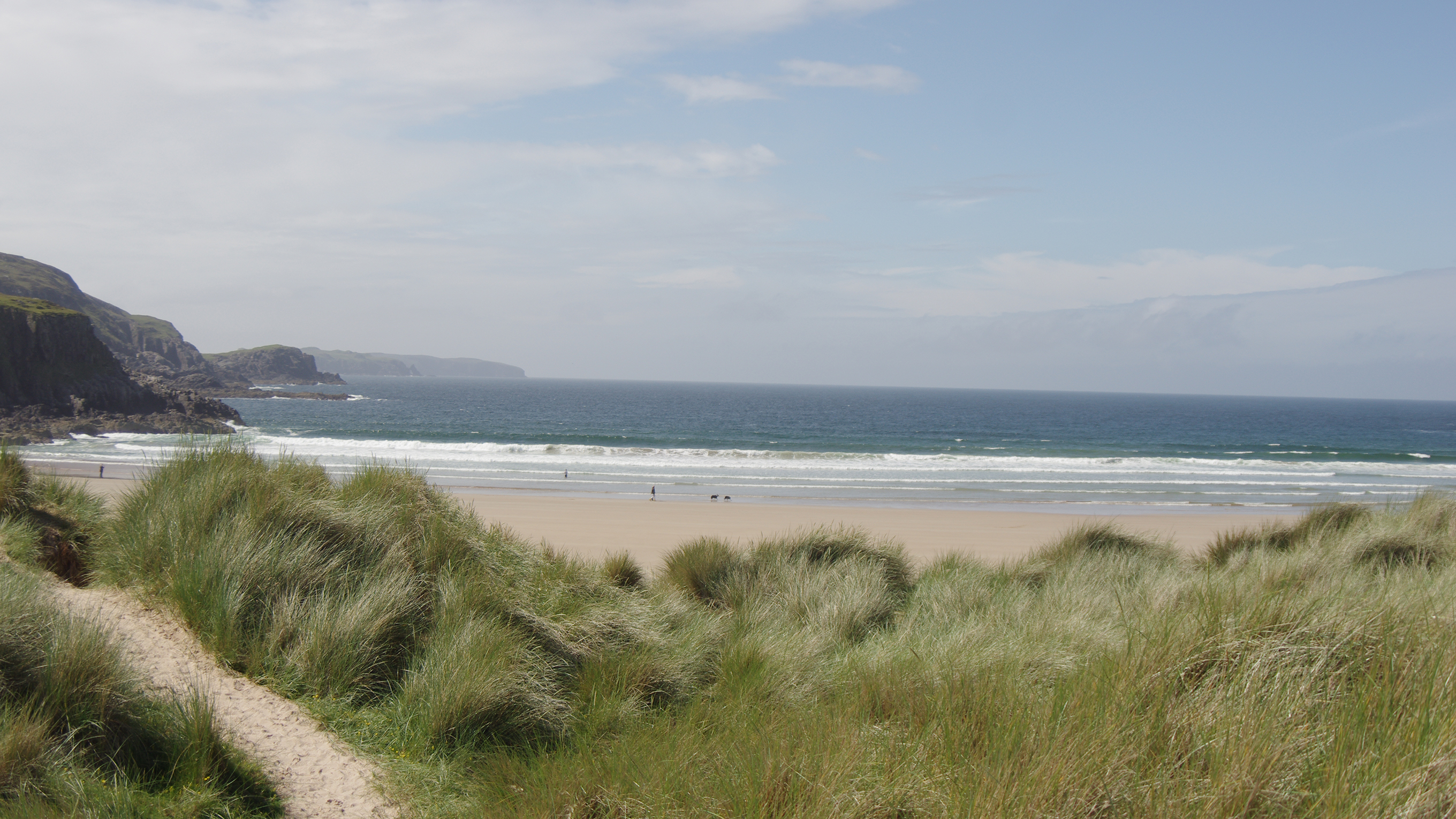 Farr Bay, with its long stretch of sand, grassy dunes, and a rocky cliff jutting out into the sea 