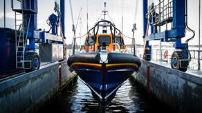 A navy blue and orange lifeboat is winched into the water at the All-weather Lifeboat Centre