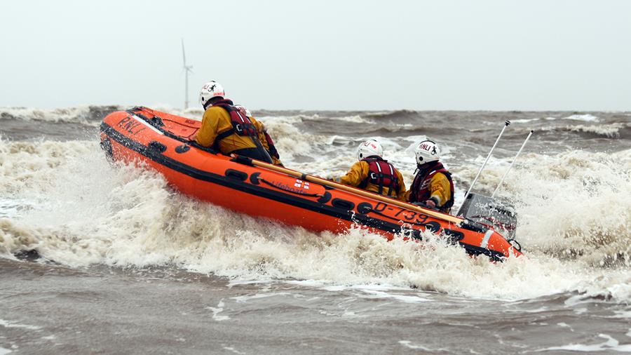Skegness’s D class lifeboat Peterborough Beer Festival IV powers through waves on a cloudy day. There are three crew members onboard the lifeboat