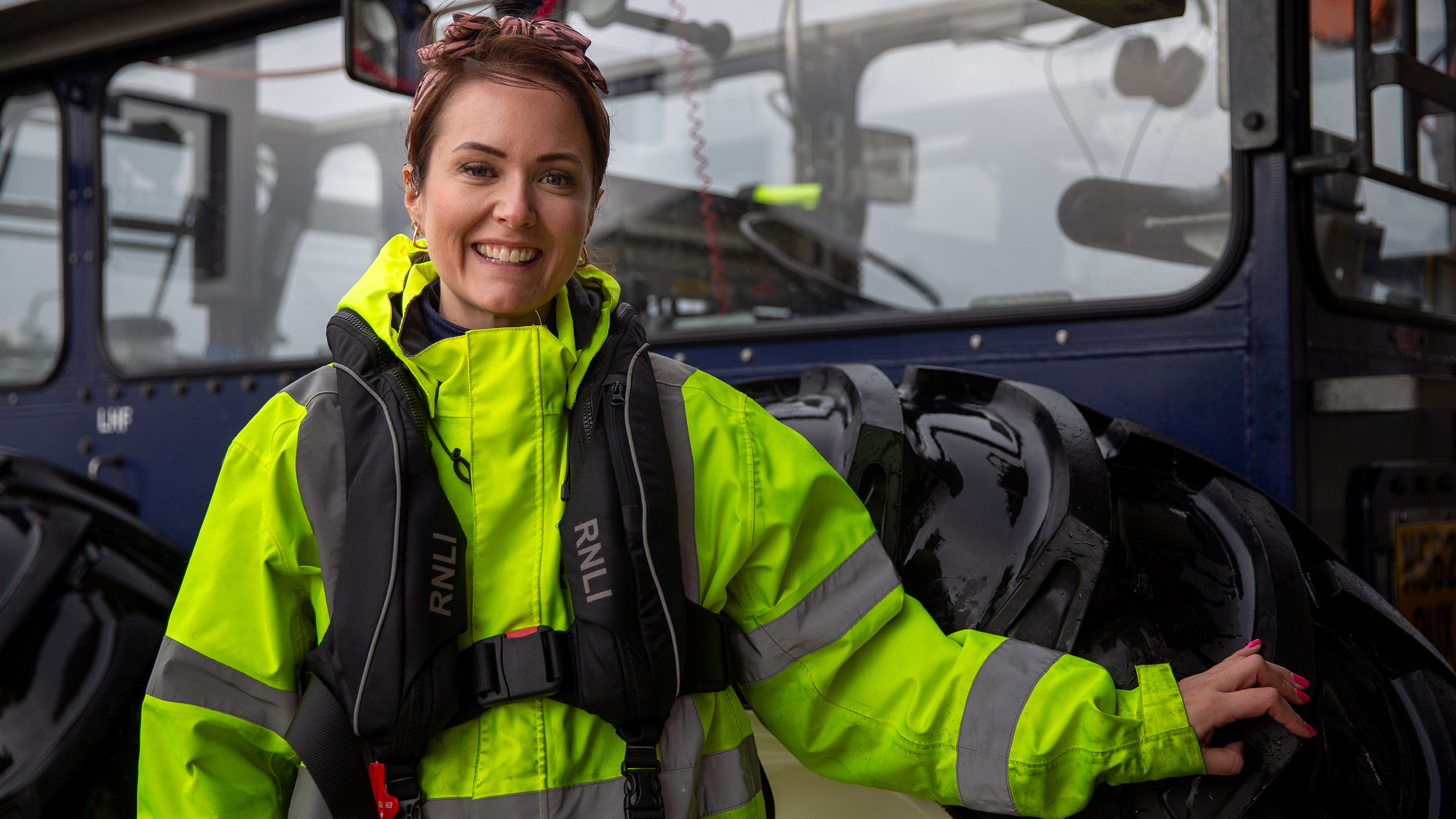 Mudeford Tractor Driver Lexi Obee-Kendall, wearing a high-vis jacket and standing in front of her station’s dark blue tractor.