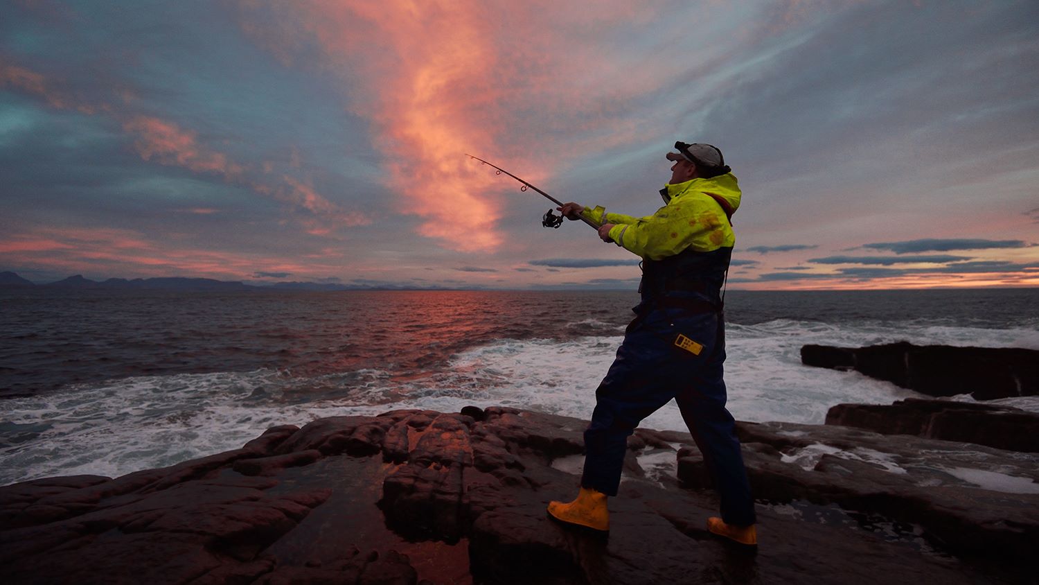 An angler fishing on rocks at sunset in Lochinver