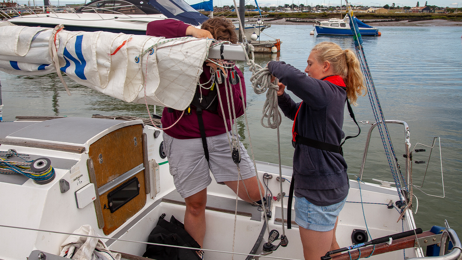 Two sailors wearing lifejackets on a small sailing boat checking their ropes.