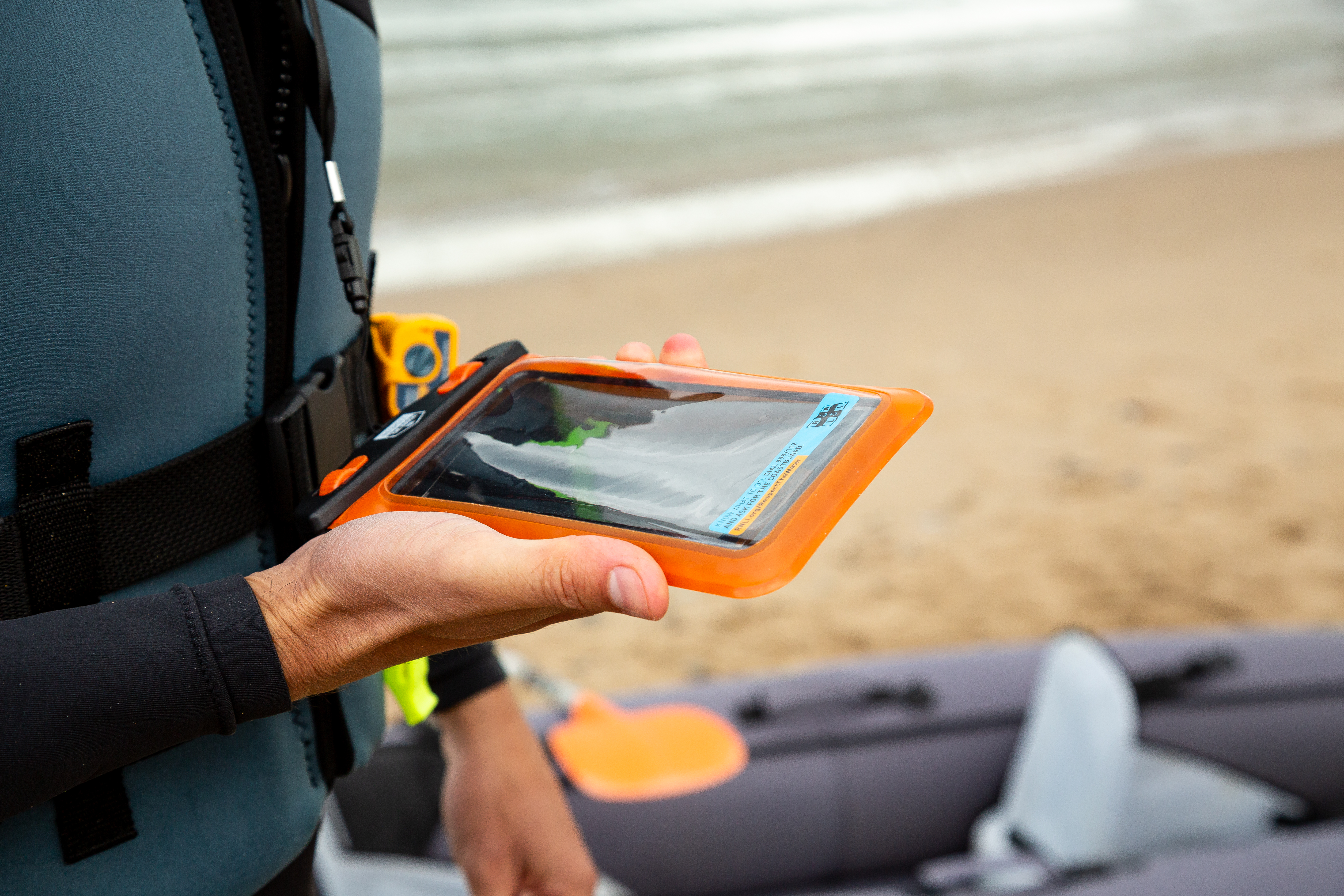 A man is holding a mobile phone in a waterproof pouch on the beach.