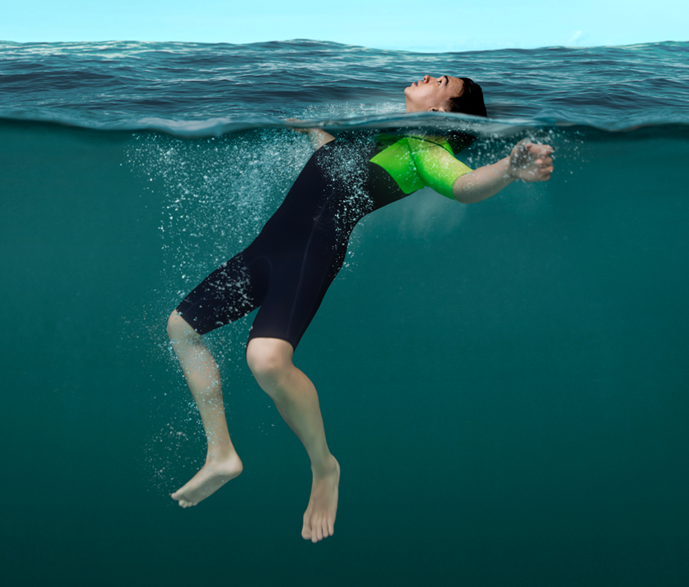 A person in a short wetsuit floats on their back with their arms outstretched and head back with their ears in the water. Their legs dangle below them.