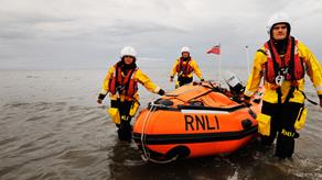 3 lifeboat crew in kit walking in water, pulling an inshore lifeboat