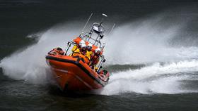 An orange lifeboat speeds across a black, rough sea.