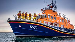 Buckie RNLI’s Severn class all-weather lifeboat on a calm sea with five crew members on deck, some looking toward the camera
