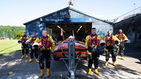 Six Dart lifeboat volunteers stood outside of the boathouse around the D class lifeboat, all wearing full crew kit