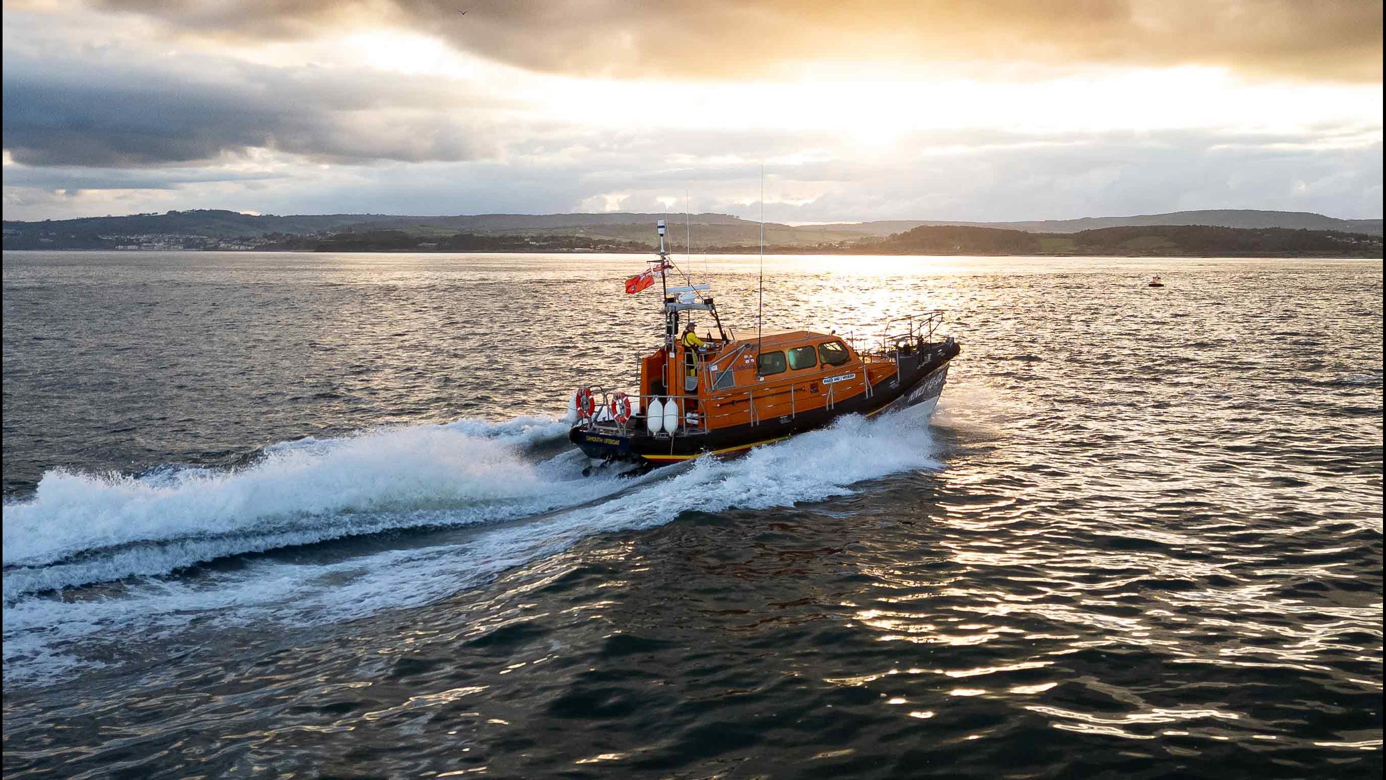 Exmouth's Shannon class lifeboat cruises along the sea at sunset on calm seas and partly clouded skies