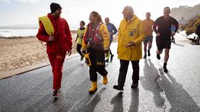 Mixed group of RNLI fundraisers walking and running on a promenade