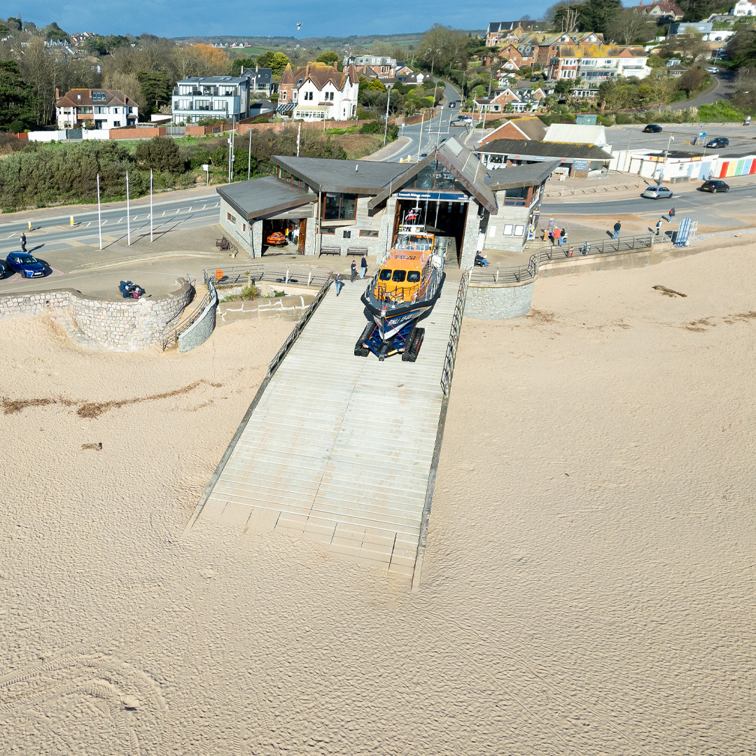 Lifeboat station with a lifeboat on a slipway leading down to a sandy beach.