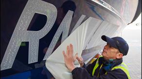 A worker applies the RNLI decal sticker with legacy names included onto the hull of a Shannon class lifeboat