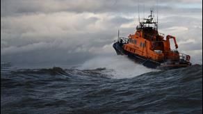 RNLI lifeboat moving through a wave towards a cloudy sky