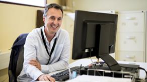 Male legacy administration team member smiling whilst sat at a computer