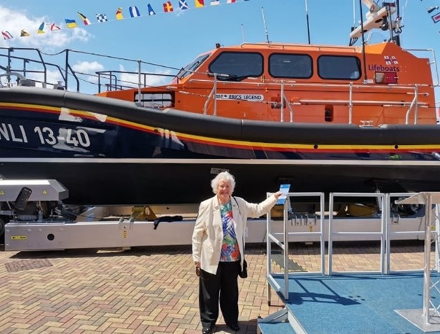 Jean Cass is stood in front of a lifeboat and smiling.