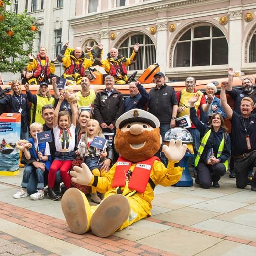 A photo of a group of RNLI crew, lifeguards, fundraisers, and supporters celebrating with Stormy Stan in front of an Atlantic lifeboat