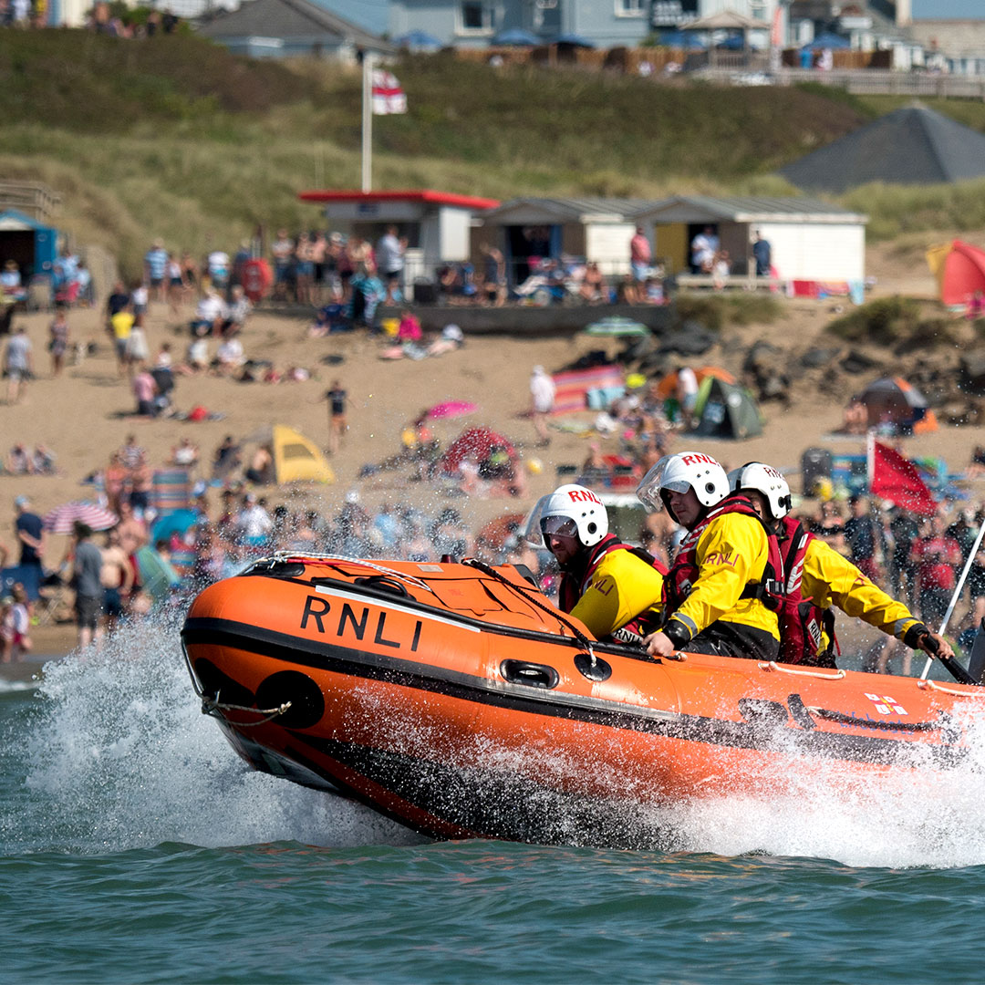 D class lifeboat with crew going to aid beach goers in the sea during busy summer season