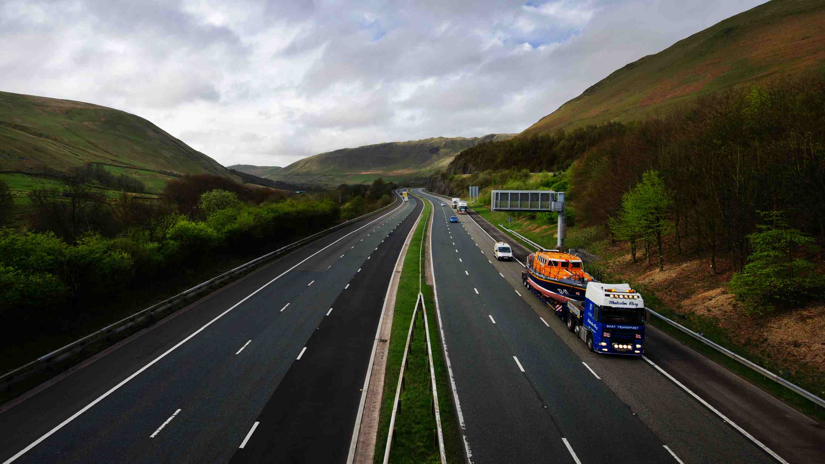 A mersey class lifeboat being transported along a motorway by lorry