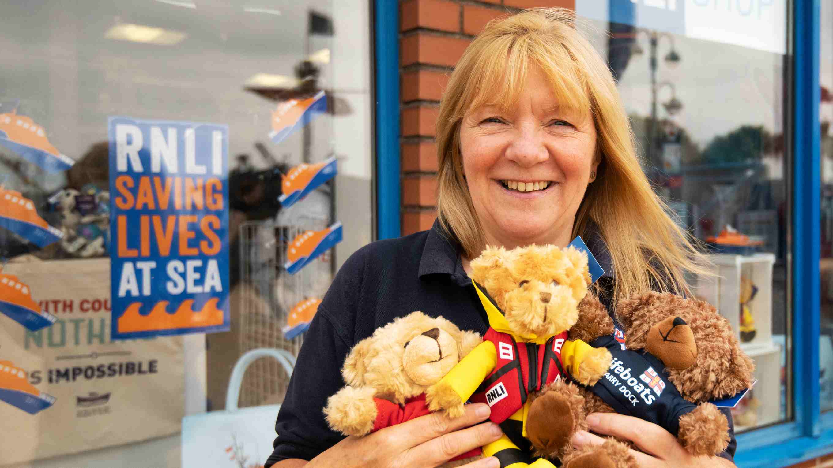 Shop Volunteer Rosemary Fisher holding teddies in front of an RNLI shop